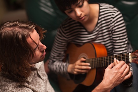 Young Male Musician Teaches Female Student How To Play the Guitar.